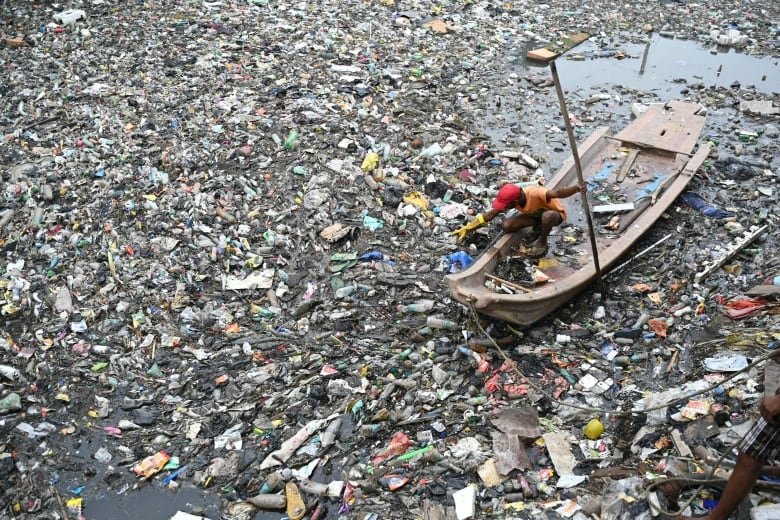 An aerial photo of a man in a boat on water that is almost completely covered in plastic.