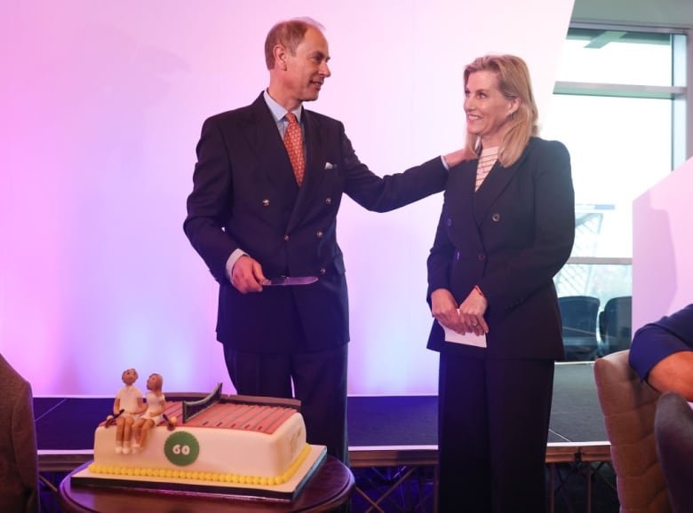 Two people stand behind a birthday cake sitting on a table.