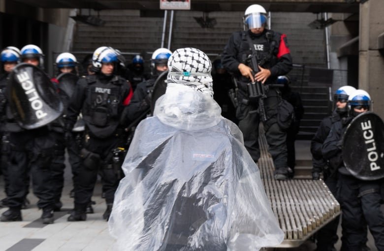 Police are seen in front of a protester wearing a scarf and plastic poncho.