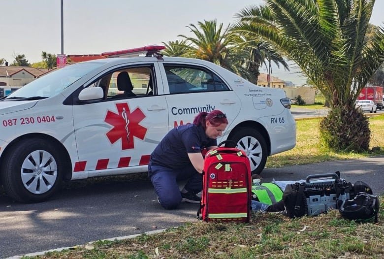 A woman kneels in front of the car to respond to an emergency.