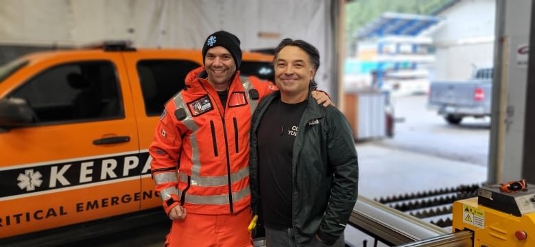 Two men stand in front of an emergency vehicle.