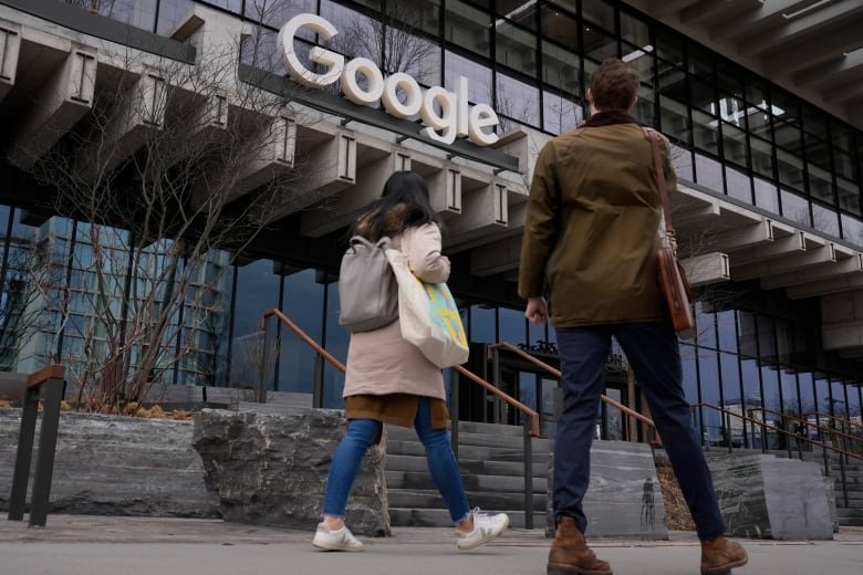 People walk into a modern office building with the word "Google" above the front door.