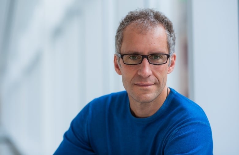 A man in a blue sweater and glasses looks to the camera.