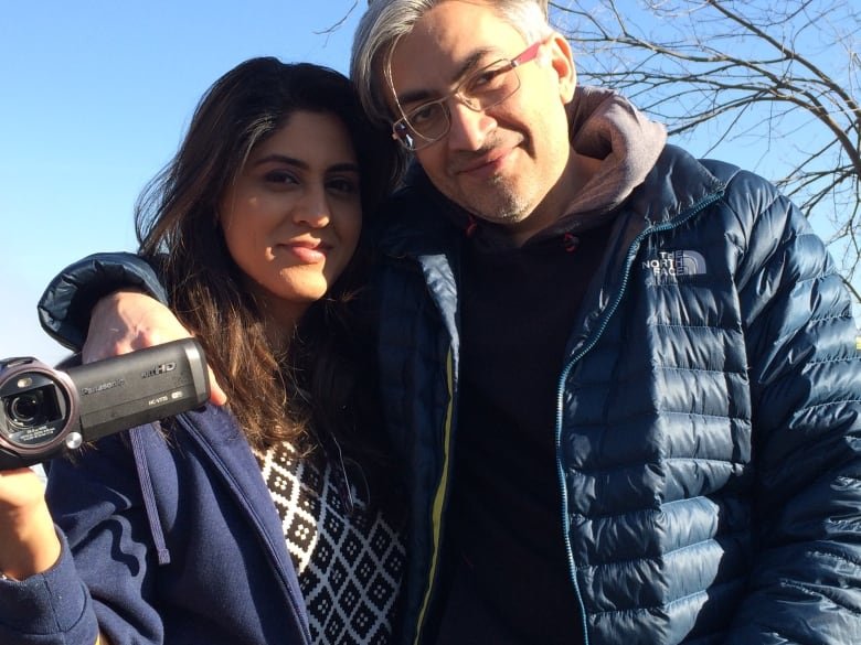 A man and a woman smile for the camera. The woman holds a camcorder in her hand.