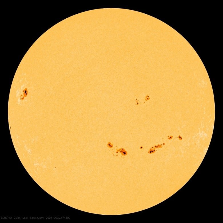 The yellow disk of the sun is dotted with several black spots.