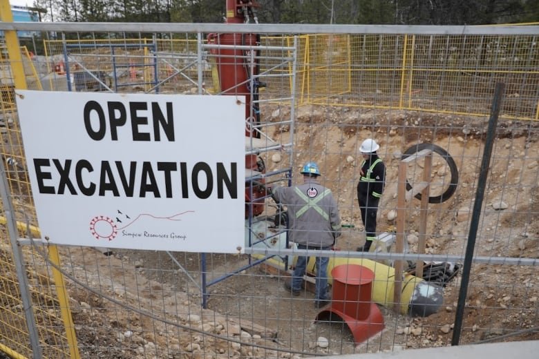 A few construction workers stand near the pipeline in an excavated area.