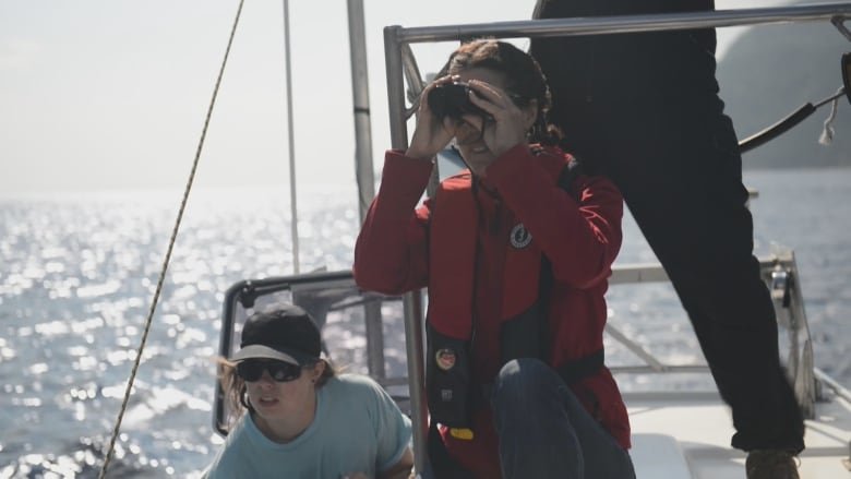 A woman on a boat looks through binoculars