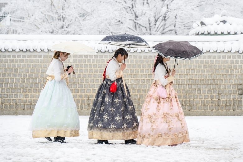 Visitors wearing traditional hanbok dresses are seen amid heavy snowfall in central Seoul.