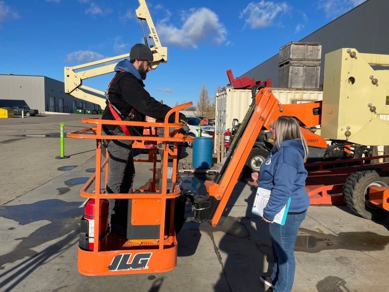 woman with clipboard watching man on bucket lift.