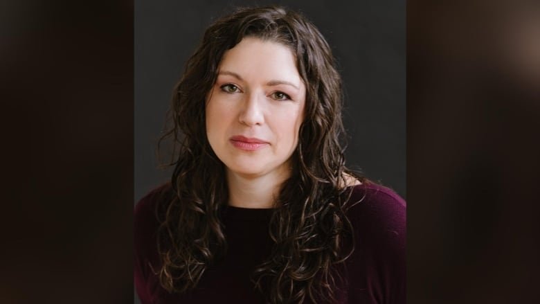 A portrait of a smiling woman with long brown hair wearing a purple sweater