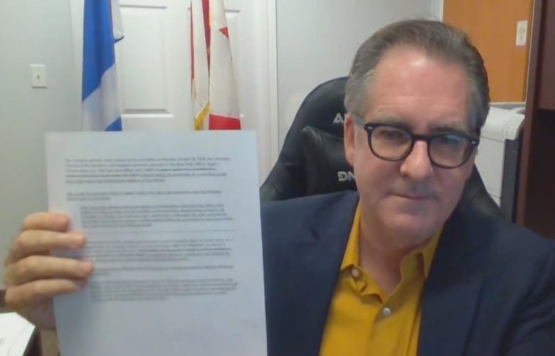 Man sitting in office holding paper up to the camera.