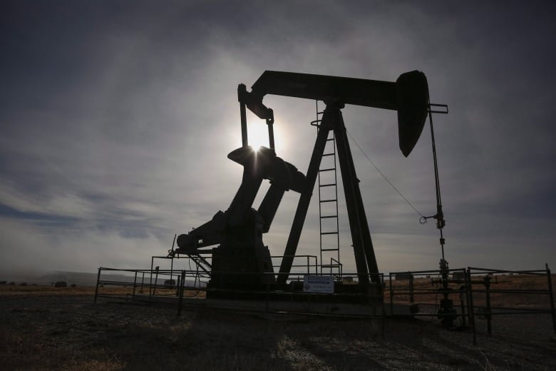 An oil pumpjack is seen in silhouette against the sun.