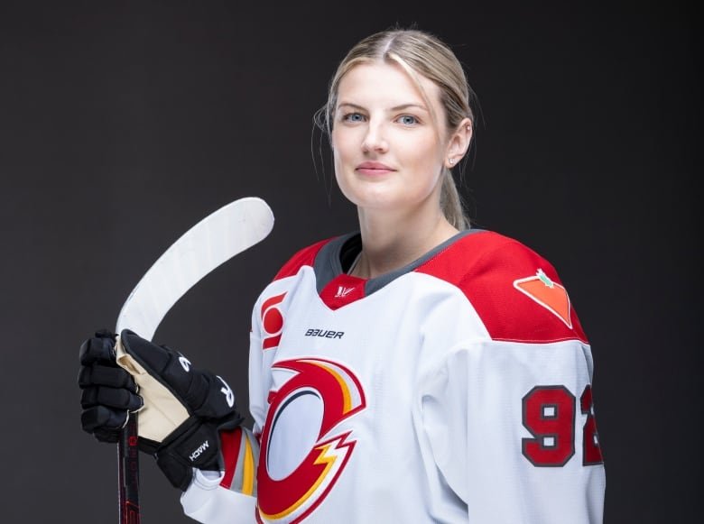 A women's hockey player wearing a jersey with a white base, with red shoulder patches, yellow, red, and light grey striping and the team's "O" logo prominently displayed on the front.