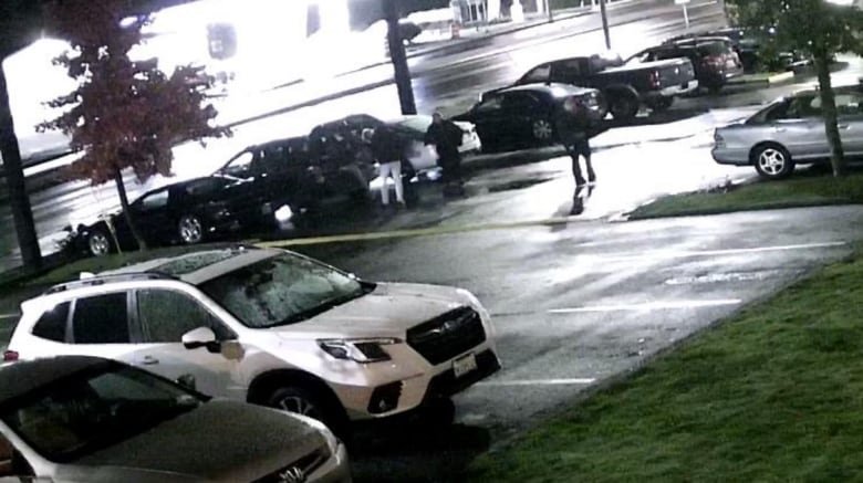 A still from surveillance footage shows a dark parking lot with three people in it.