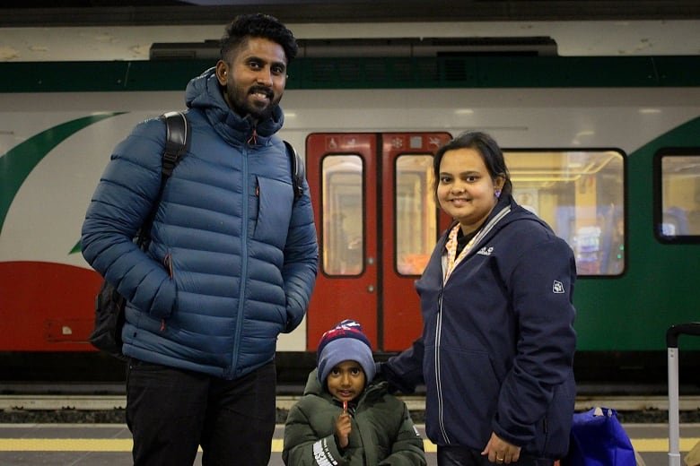 A father and mother stand with their child on a railway platform.