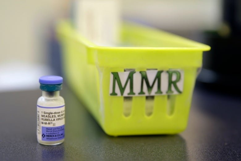 A vaccine vial is shown to the left of a bin labelled "MMR" on a countertop.