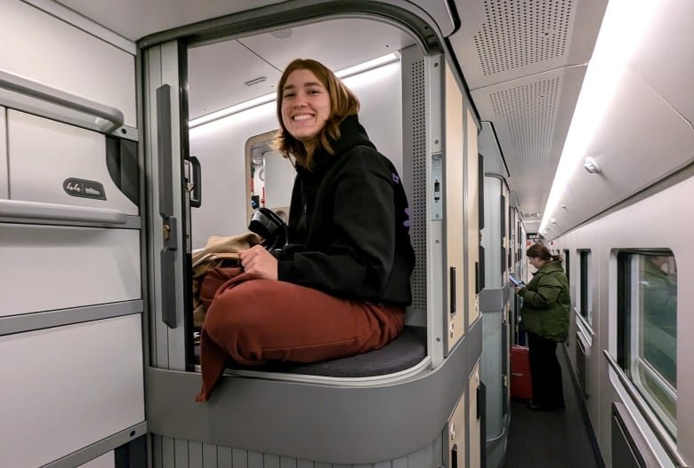 A young person sits on the top of a bunk bed in a sleeper train.