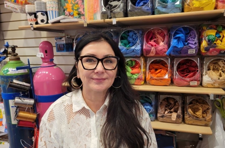 A woman stands next to a wall filled with containers of colourful, deflated balloons.