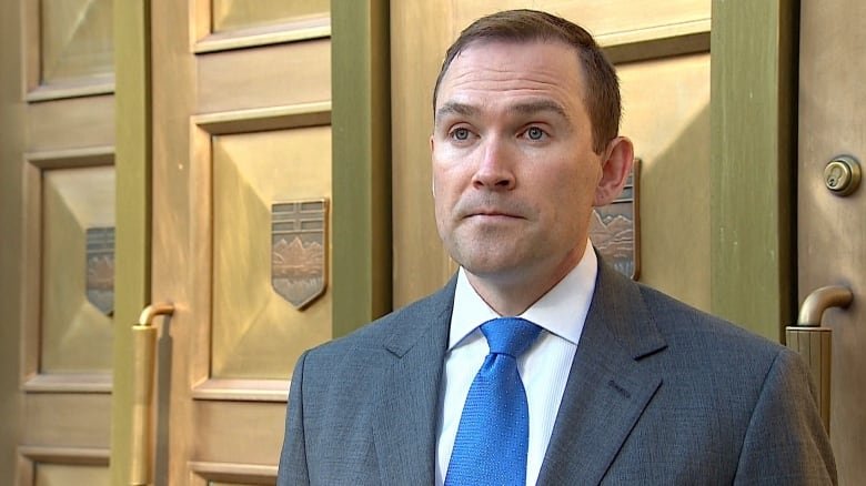 A man stands in front of a gold courtroom door.