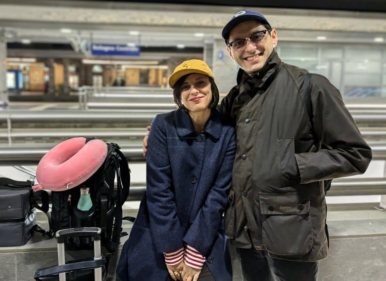 A couple standing on a train platform, smiling.