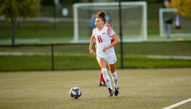 A women's soccer player runs with the ball at her feet.