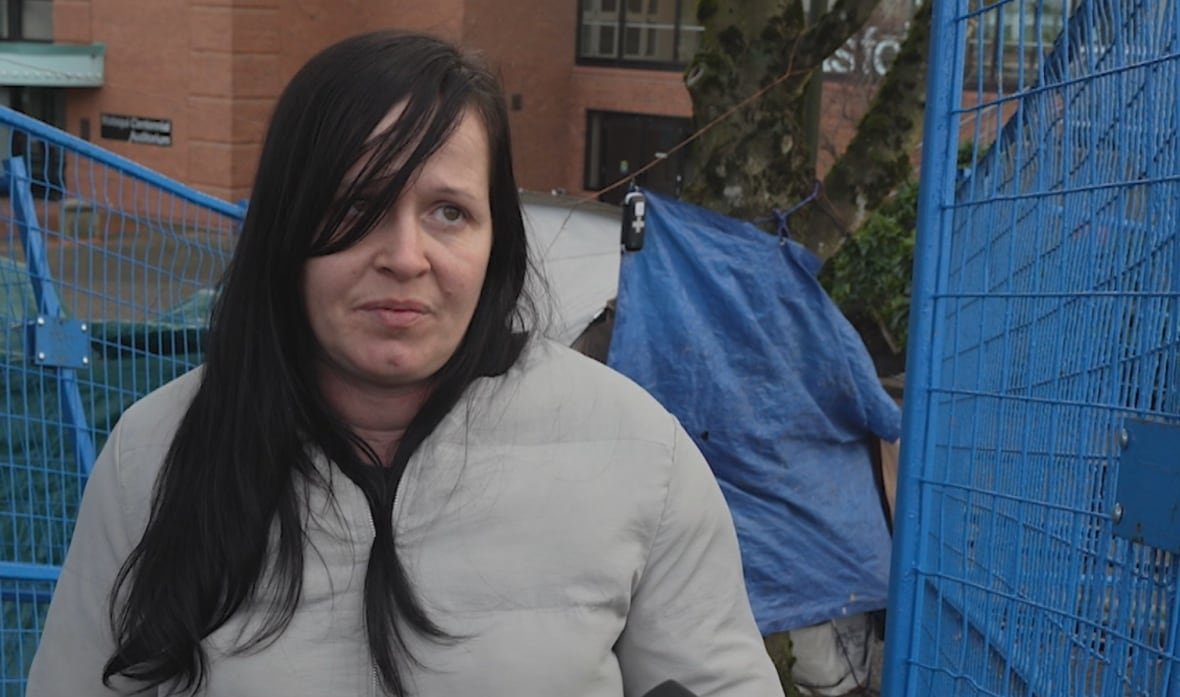 An unhappy woman with a sad face in a grey, insulated jacket with dark hair speaks to a reporter.