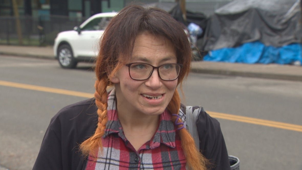 A woman in a plaid shirt and wearing glasses speaks with a reporter.