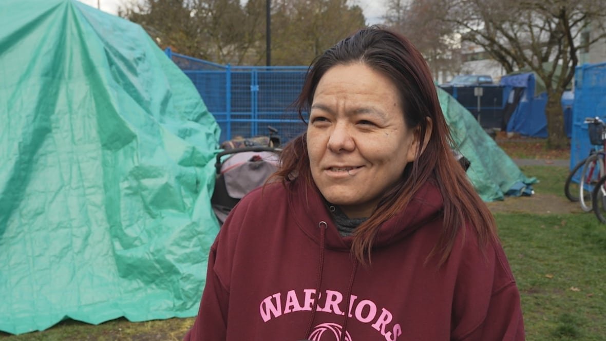 A woman with a dark, wine-coloured sweater speaks with a reporter.