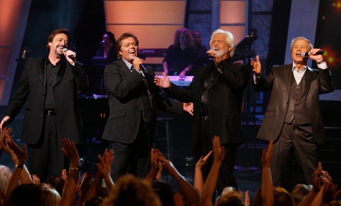 osmonds Four men sing on stage wearing suits.