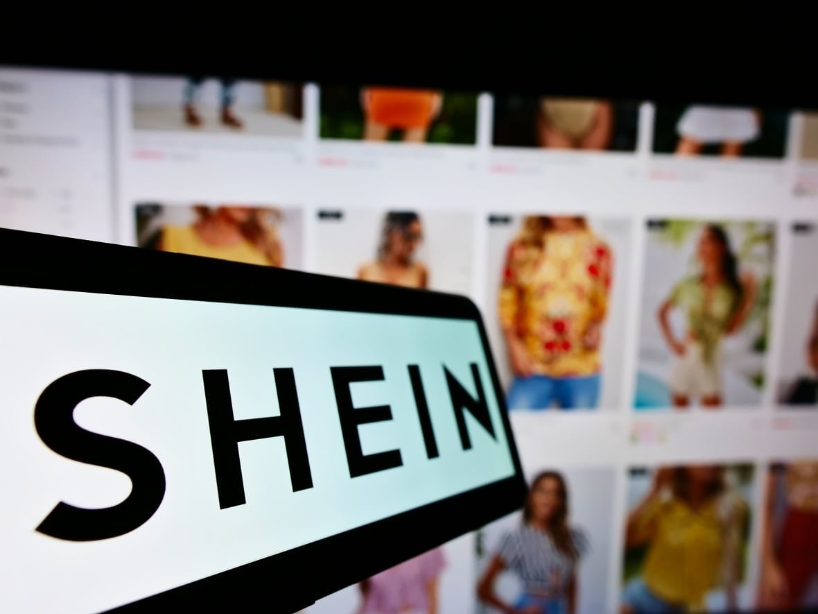 2037893222 A mobile phone with the logo of Chinese e-commerce company Shein on screen in front of a business website.
