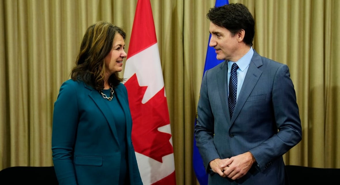 alta-immigration-20240327 A woman with medium-length brown hair and a teal-coloured suit smiles as a tall brunette man wearing a blue suit.