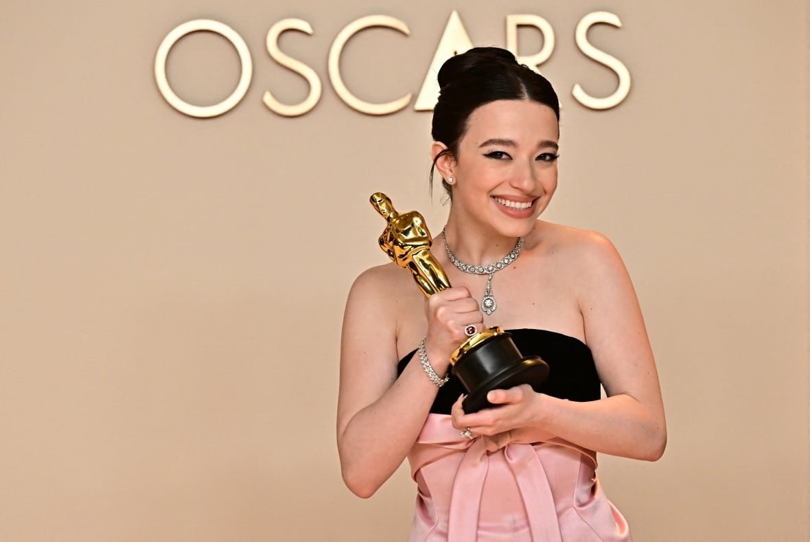 2202474104 A smiling woman poses with a trophy in front of the word Oscars.