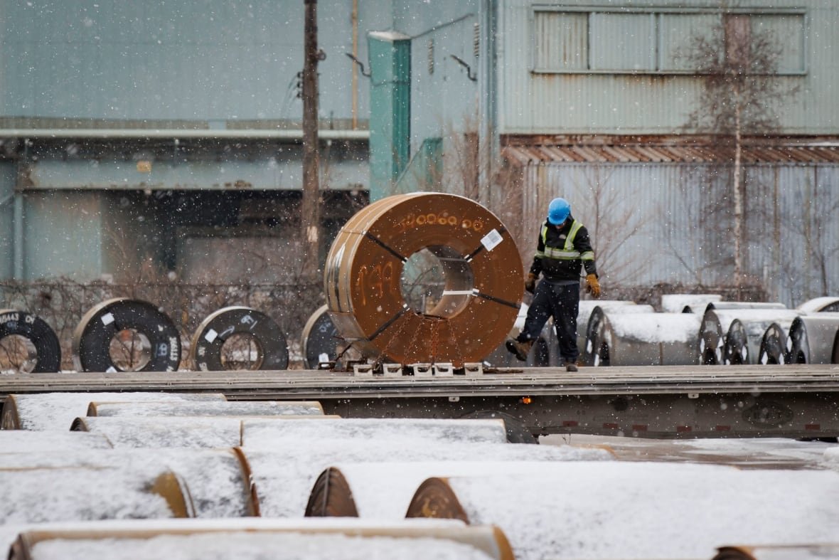 hamilton-steel A worker stands next to large steel rolls outside.