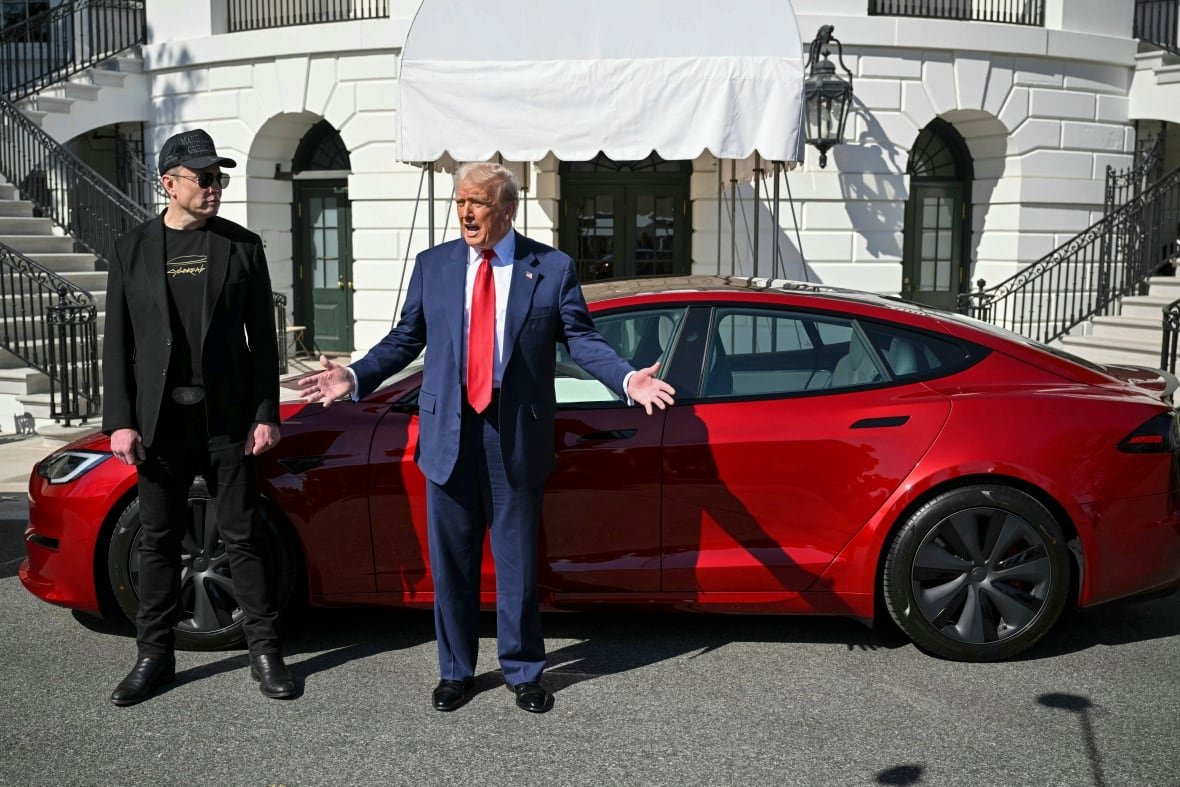 trump-1 Two men stand in front of a red car.