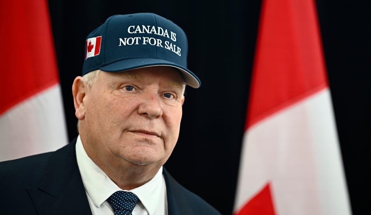 elxn-ont-preparedness-20250126 A man is shown from the shoulders up wearing a suit and a blue hat that says "Canada is not for sale."