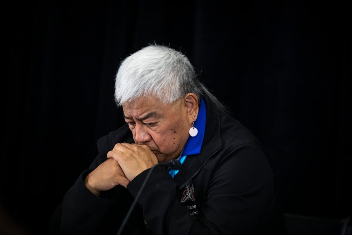 fnha An Indigenous man bends his head over clasped hands.