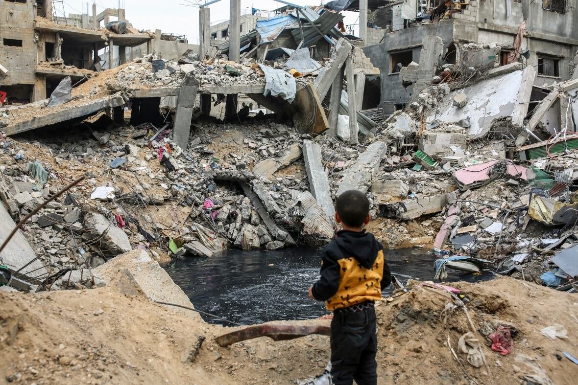 israel-gaza-2 A little boy, pictured from behind, stands in front of a massive pile of rubble.