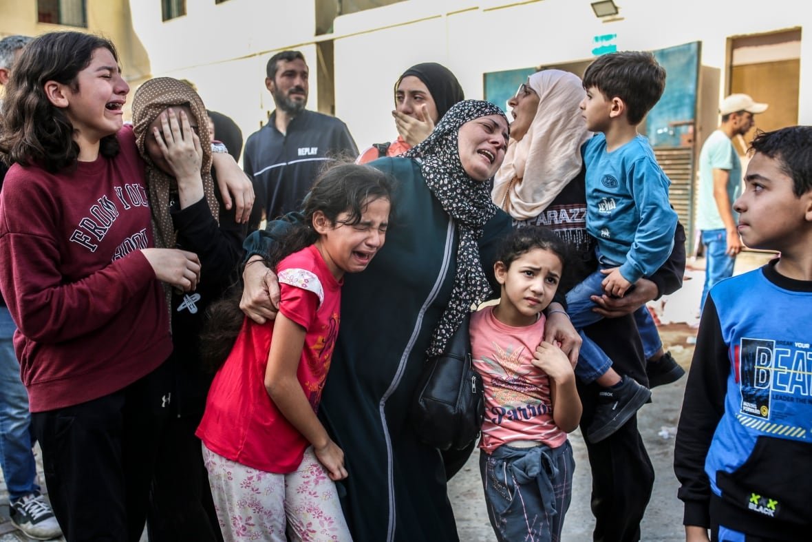 israel-gaza-49 A group of women, children and men stand in the streets crying and screaming as they look toward something off camera.