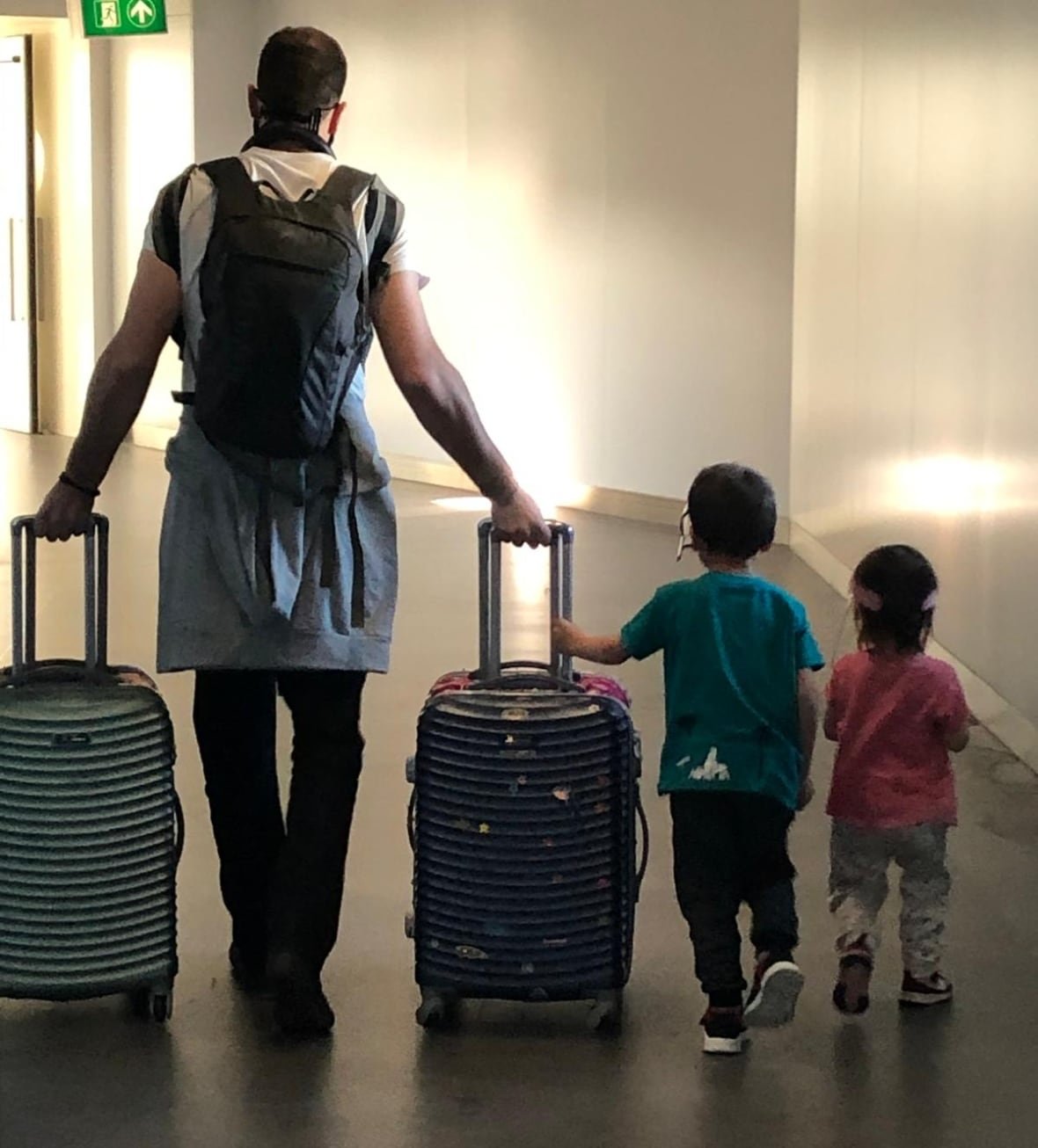 jacques-neuhoff-walking-with-his-two-children-in-the-airport A man and two children walk away in an airport rolling luggage.