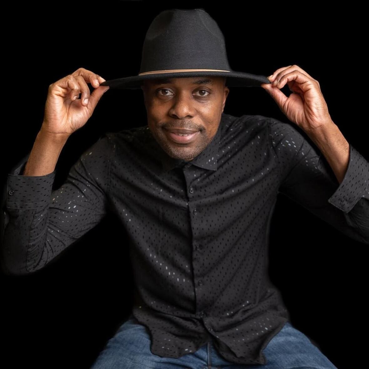 malik-shaheed-1 A man posing for a photo with his hand on his hat.