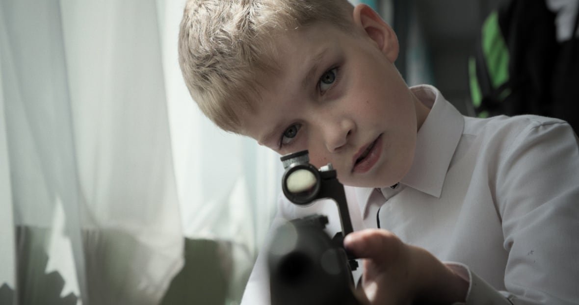 mr-nobody-against-putin A young boy looks through the sites of a rifle, pointed directly at the camera.