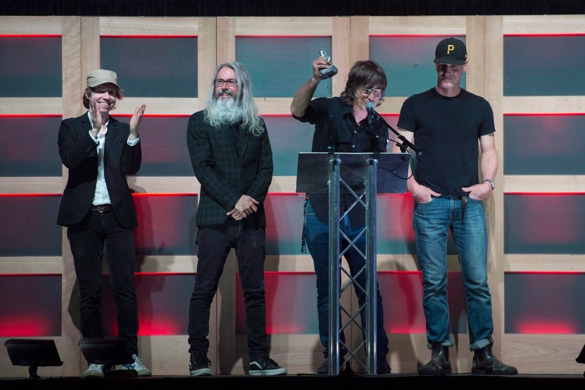 Four men are shown on a stage as one holds up an award.