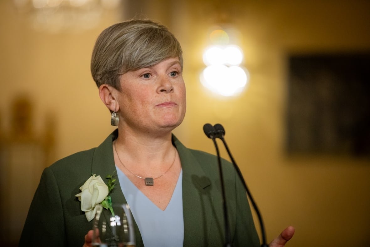 new-bc-ndp-government-cabinet-members-josie-osborne-1 A white woman with short hair and hooped earrings speaks to a mic.