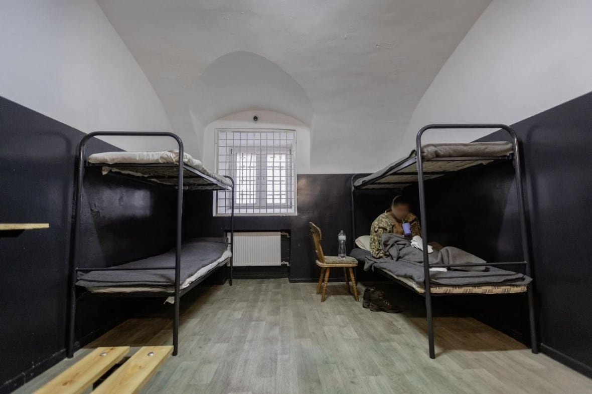 north-korean-pow Bunk beds in a room. On the bottom left bed, a soldier is seen drinking from a cup. His face has been blurred.