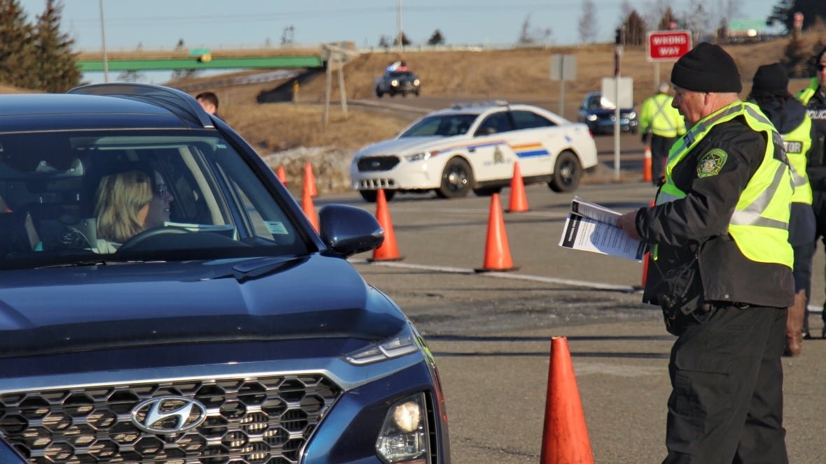 nova-scotia-border-stops An official wearing a safety vest speaks with the driver of a vehicle who is trying to enter Nova Scotia from New Brunswick.