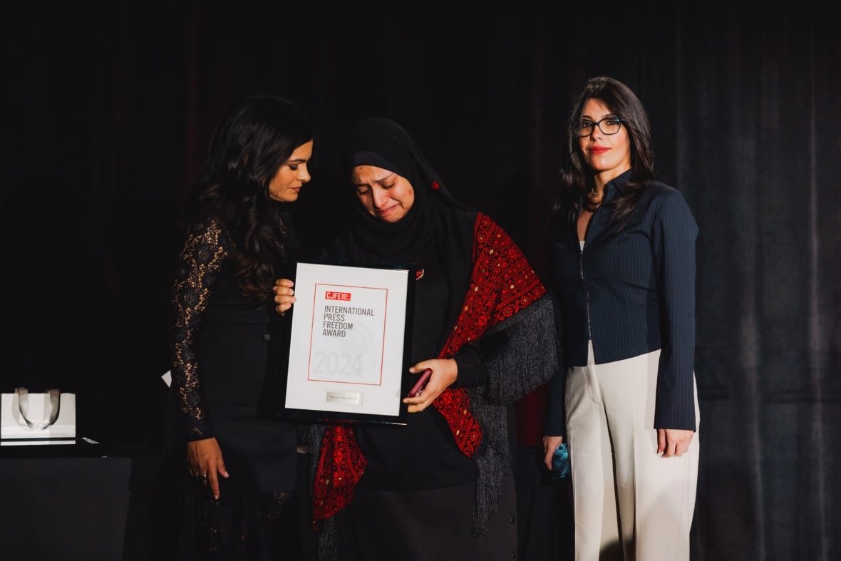 samar-abu-elouf-1 A crying woman in a hijab holds stands flanked by two other woman as she holds up a framed piece of paper with the words: " International Press Freedom Award."