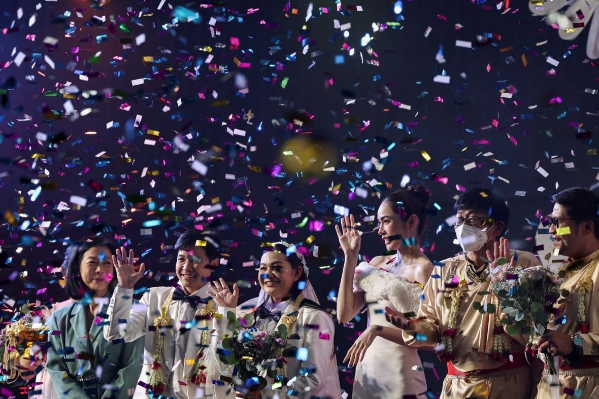 thailand-lgbt Couples dressed for weddings smile and wave as confetti fills the air.