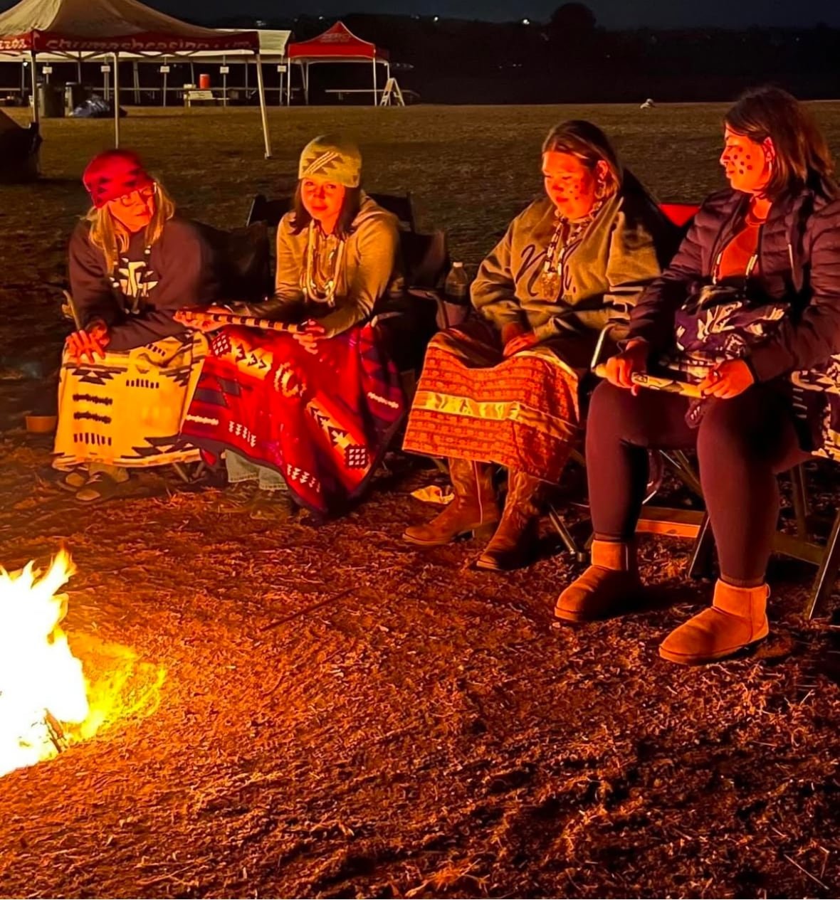 women-around-the-fire Four women gather around a fire wearing skirts and wrapped in blankets to keep warm.
