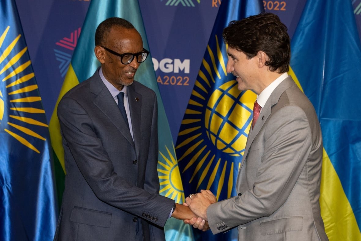 1404833377 A bespectacled dark complected man in a suit and tie and a light beard shakes hands with a dark haired clean shaven Caucasian man in a suit and tie, with flags behind them.