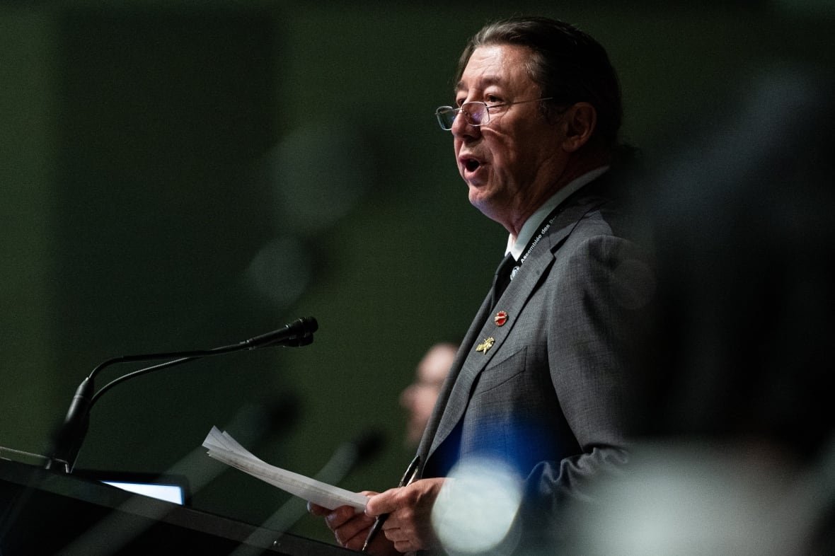 Senator Paul Prosper speaks during a plenary session on economic reconciliation the first day of the Assembly of First Nations. He is shown in profile at a podium wearing a grey suit, white shirt and dark tie.
